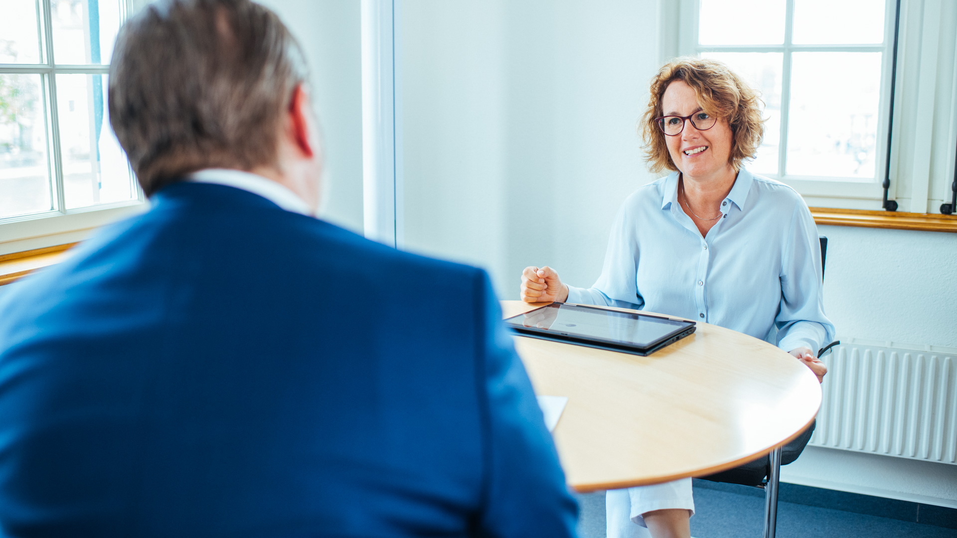 mpw Coaching Frau sitzt am Tisch, lächelt und hört zu